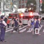無関心な歩行者が横断する間を緊急走行する救急車と行先を見守る警察官　渋谷スクランブル交差点より